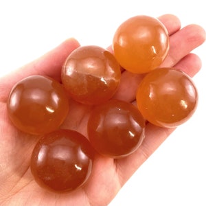 May include: Six smooth, polished orange carnelian spheres. The spheres are approximately the same size and are arranged in a cluster.