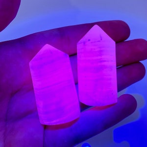 May include: Two pink and white striped crystal points glowing under a black light. The points are about 2 inches tall and have a smooth, polished finish.