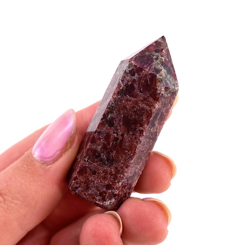 May include: A deep red and green crystal point, also known as a red and green  pyrite, is held in a hand. The crystal is smooth and polished, with a pointed tip.