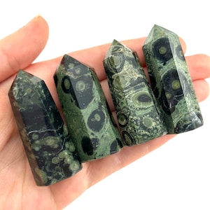 Pode incluir: Quatro pontas de pedra serpentina verde e preta, também conhecidas como serpentina verde, estão dispostas em fila. As pontas são polidas e têm um acabamento liso e brilhante.