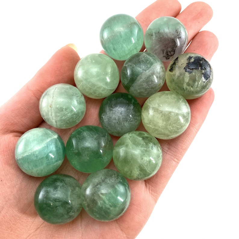May include: A collection of green fluorite spheres, ranging in size and shade, with some showing a slight translucence. The spheres are smooth and polished, with a natural, earthy appearance.