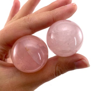 May include: Two smooth, pink rose quartz spheres. The spheres are polished and translucent, with a slight shimmer.