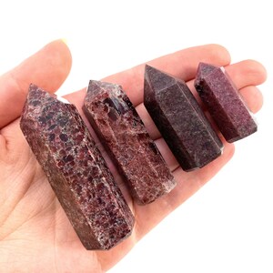 May include: Four red and brown gemstone points, also known as red and brown crystal wands, are arranged in a row on a hand. The points are different sizes and have a natural, rough texture.