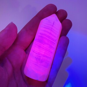 May include: A pink and white crystal point with striations, glowing under a black light.