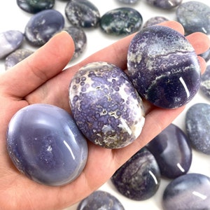May include: A collection of polished purple agate stones with various patterns and textures. The stones are smooth and have a natural, earthy look.