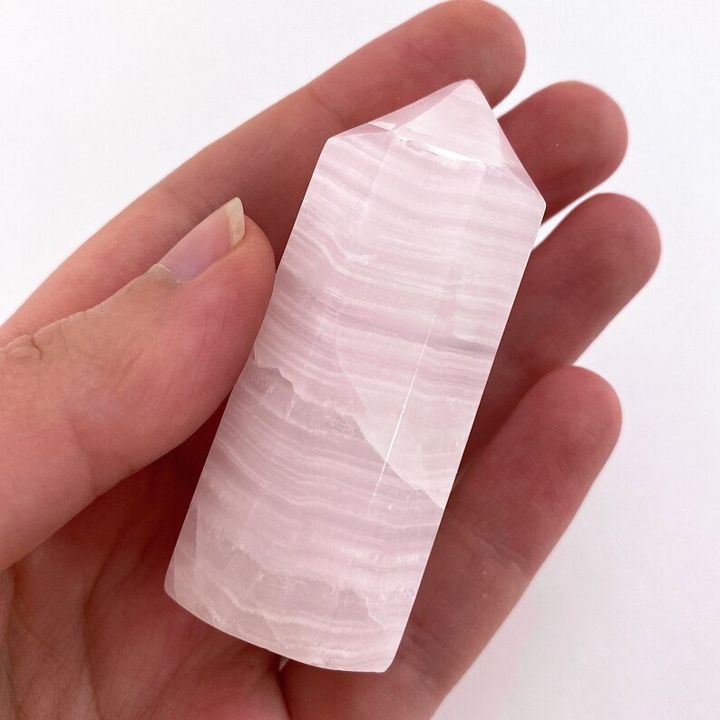 May include: A pink selenite crystal tower with white striations. The tower is smooth and polished.