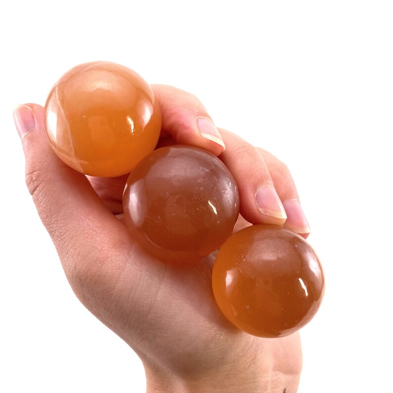 May include: Three smooth, orange-colored spheres made of polished stone. The spheres are arranged in a stack, with the largest sphere on the bottom and the smallest sphere on top.
