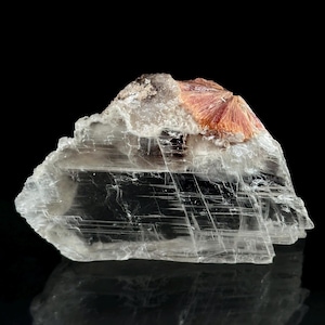 May include: A translucent, layered mineral specimen with a fan-shaped cluster of reddish-pink crystals. The mineral has a crystalline structure and sits against a black background, showcasing its natural beauty.