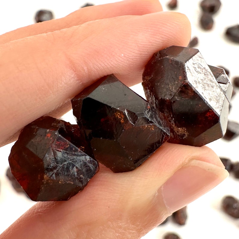 May include: Three dark brown, faceted, and translucent crystals with a slightly metallic sheen. The crystals are held in a hand.