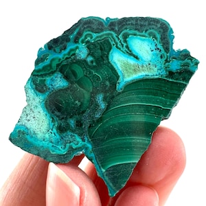 May include: A vibrant, polished malachite stone with swirling patterns of deep green and turquoise. The natural gemstone displays a layered, banded appearance, showcasing its unique mineral formations. The stone is held in a hand, highlighting its size and texture.