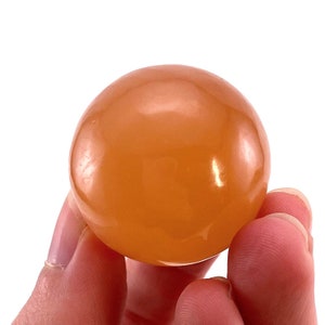 May include: A smooth, polished orange carnelian sphere. The sphere is approximately 2 inches in diameter and has a warm, translucent color.