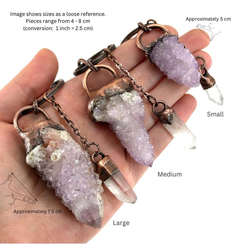 May include: Three crystal pendants of varying sizes, each with a unique shape and color. The pendants range from 4 to 8 cm in length. The crystals are attached to a copper-colored metal ring and chain. The image includes text indicating the sizes.