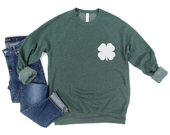 May include: A green sweatshirt with a white four-leaf clover graphic on the front.