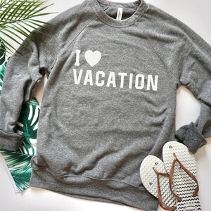 Puede incluir: Sudadera gris con texto blanco que dice "Me encanta la vacación" con un símbolo de corazón.