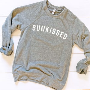 May include: A gray sweatshirt with the word "SUNKISSED" printed in white on the front.