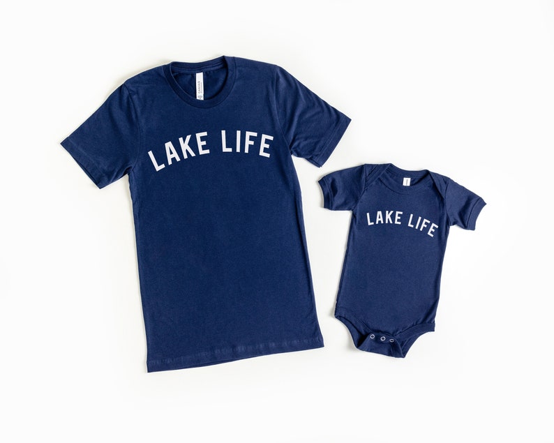 Puede incluir: Dos camisas azul marino con el texto "LAKE LIFE" en blanco. La camisa m&aacute;s grande es una camiseta y la camisa m&aacute;s peque&ntilde;a es un body.