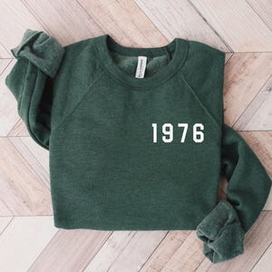 May include: A dark green sweatshirt with the year 1976 printed in white on the front.