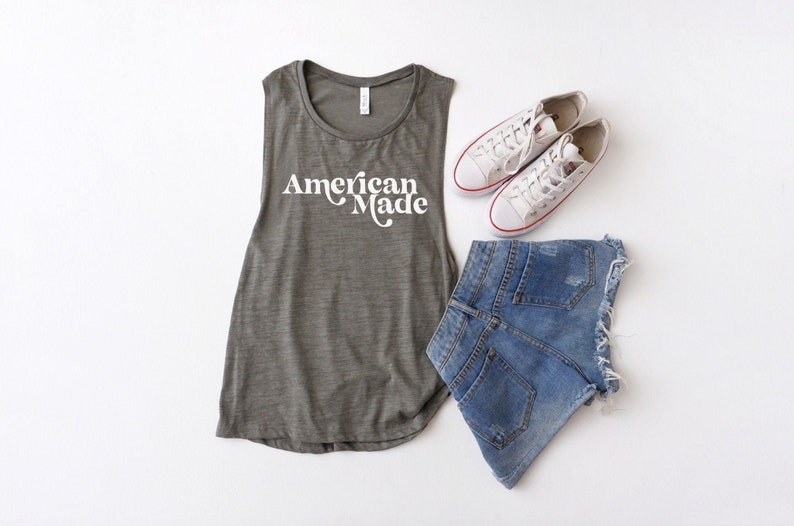 May include: A green tank top with the text "American Made" in white. The tank top is paired with denim shorts and white sneakers.