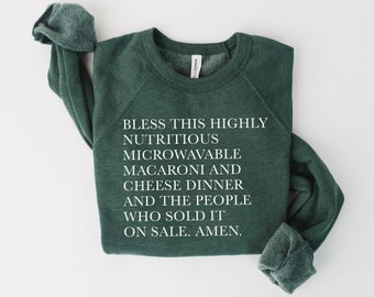May include: A dark green sweatshirt with white text that reads "Bless this highly nutritious microwavable macaroni and cheese dinner and the people who sold it on sale. Amen."