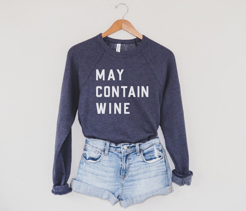 Puede incluir: Una sudadera azul marino con el texto "MAY CONTAIN WINE" impreso en blanco en la parte delantera. La sudadera se est&aacute; modelando con unos pantalones cortos de mezclilla azul claro.