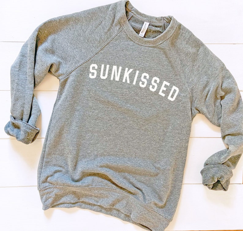 May include: A gray sweatshirt with the word "SUNKISSED" printed in white on the front.