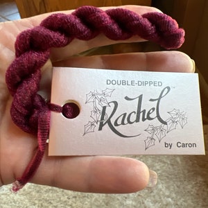 May include: A close-up of a burgundy yarn ball with a white tag that reads "DOUBLE-DIPPED Rachel by Caron".