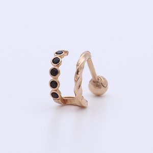 May include: A gold-colored earring with a curved design. The earring features a row of five small black stones along the curve and a small ball at the end of the post. The post has a textured design.