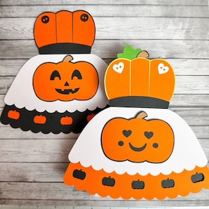 May include: Two orange pumpkin-shaped Halloween decorations with white and black accents. The pumpkins have different facial expressions. One pumpkin has a happy face with a wide smile and the other pumpkin has a smiling face with hearts for eyes.