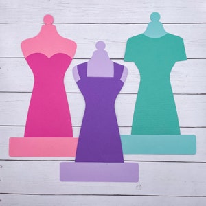 May include: Three paper dress forms with different colored dresses. The dress forms are pink, purple, and teal. The dresses are all different styles.