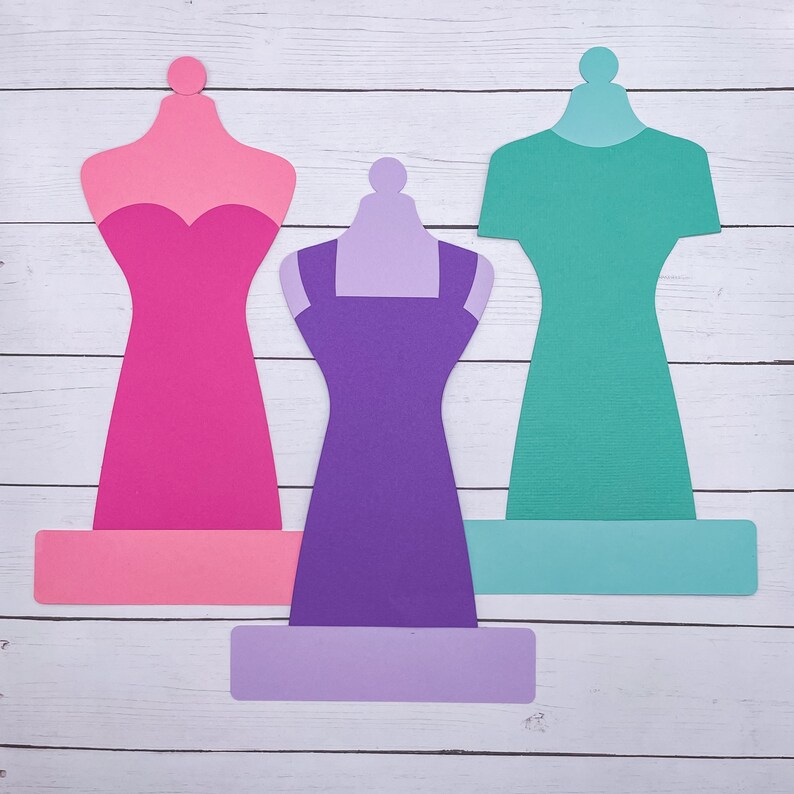 May include: Three paper dress forms with different colored dresses. The dress forms are pink, purple, and teal. The dresses are all different styles.