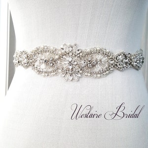 Op de afbeelding: Een witte bruidsgordel met kralen en strass met een bloemenpatroon. De gordel is op een wit mannequin.
