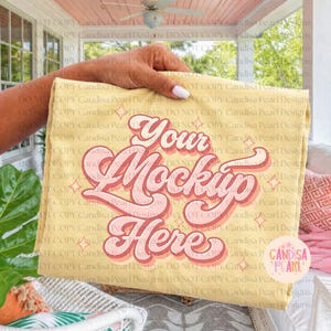 May include: A yellow rectangular item with the text "Your Mockup Here" in a retro font. The text is in shades of pink and red with a shadow effect. The item is held by a person.