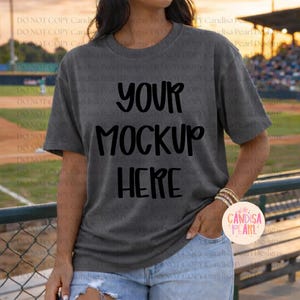 May include: Dark gray t-shirt with the text "YOUR MOCKUP HERE" in black. The shirt is a short-sleeved, crew neck style. The image is a mockup, perfect for showcasing designs. The model is wearing blue jeans and a bracelet.
