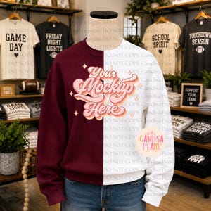 Op de afbeelding: Een tweekleurige sweater met ronde hals, met een donkerrode linkerkant en een witte rechterkant. In het midden staat de tekst Your Mockup Here in een retro, meerlaags roze en oranje scriptlettertype, geaccentueerd door kleine sterretjes.