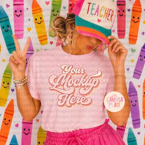 May include: A light pink t-shirt featuring the text Your Mockup Here in a retro-style font with star accents. The shirt is worn with a multi-colored trucker hat with the word TEACHER printed on the front and a pink skirt with an elastic waistband.