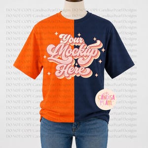 May include: A split-colour t-shirt featuring a bright orange left side and a dark navy blue right side. The centre displays the text Your Mockup Here in a layered, retro-style font with pink and cream tones, accented by small four-pointed stars.