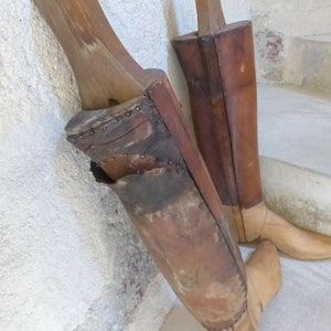 May include: Two wooden boot forms, one brown and one tan, with leather coverings. The forms are used to shape boots during the manufacturing process.