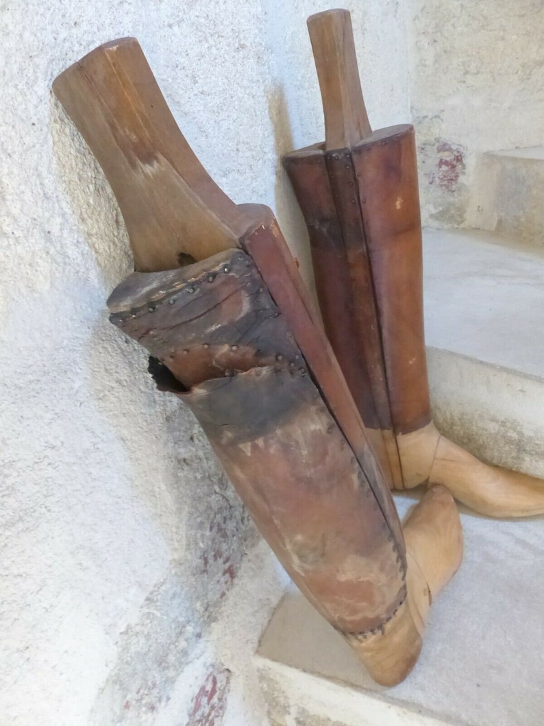 May include: Two wooden boot forms, one brown and one tan, with leather coverings. The forms are used to shape boots during the manufacturing process.