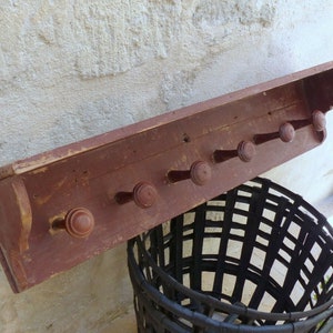 Peut inclure: Un porte-manteau en bois rustique avec une étagère et six chevilles en bois. Le porte-manteau est peint en rouge foncé et a une finition vieillie.