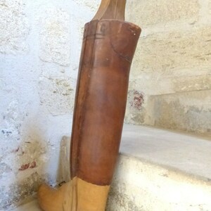 May include: A wooden boot last with a brown leather covering. The last is made of wood and has a light brown finish. The last is used to shape boots during the manufacturing process.