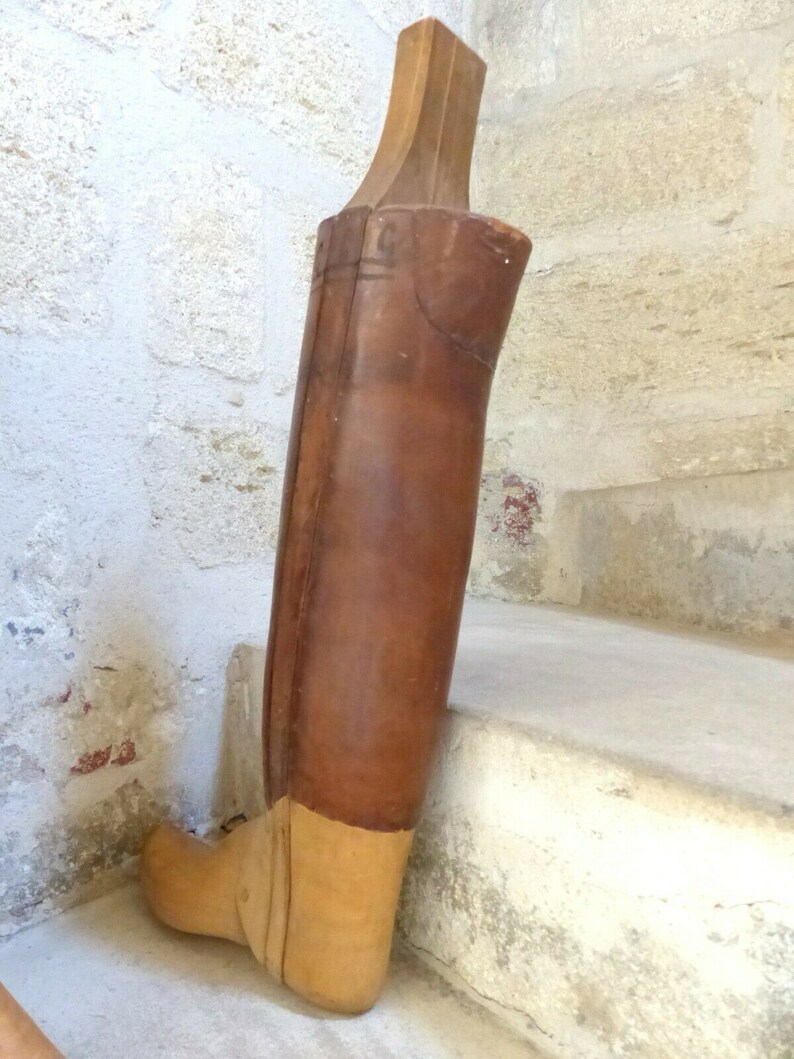May include: A wooden boot last with a brown leather covering. The last is made of wood and has a light brown finish. The last is used to shape boots during the manufacturing process.
