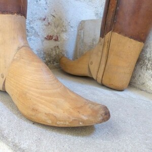 May include: A pair of wooden shoe lasts with leather tops. The lasts are made of light brown wood and have a pointed toe. The leather tops are a darker brown and have a worn look.