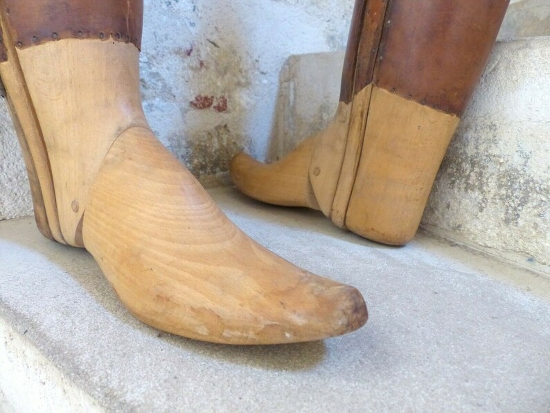May include: A pair of wooden shoe lasts with leather tops. The lasts are made of light brown wood and have a pointed toe. The leather tops are a darker brown and have a worn look.