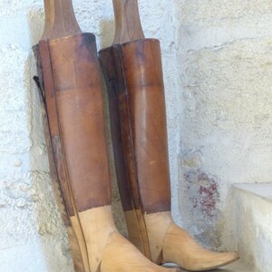 May include: Two wooden boot forms with brown leather coverings. The forms are made of wood and have a rounded toe. The forms are on a stone step.