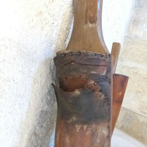 May include: A close-up of a brown leather boot with a wooden top. The boot is worn and has been repaired with metal rivets. The boot is hanging on a wall.