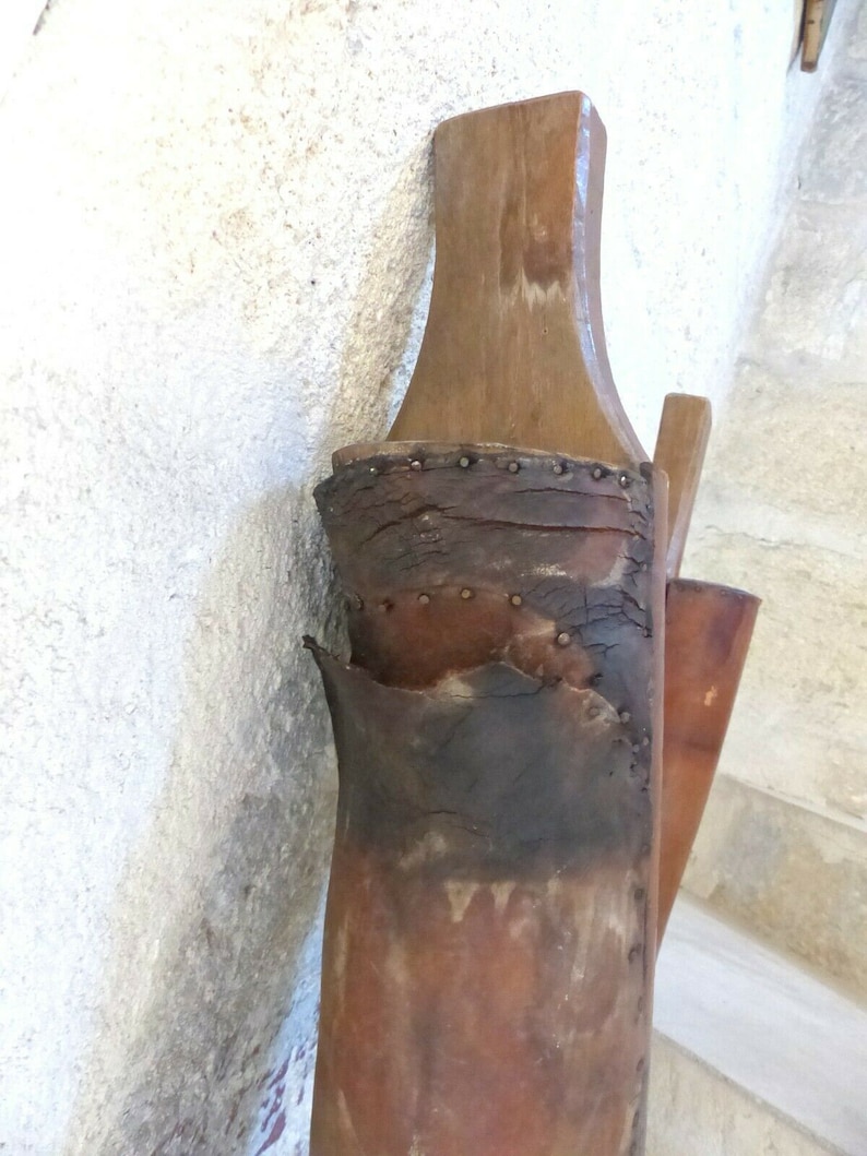May include: A close-up of a brown leather boot with a wooden top. The boot is worn and has been repaired with metal rivets. The boot is hanging on a wall.