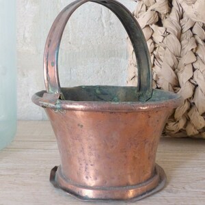 Peut inclure: Un petit pot en cuivre avec une base arrondie et une seule poignée. Le pot a un aspect usé et vieilli et est parfait pour présenter de petites plantes ou des fleurs.