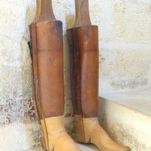 May include: Two wooden boot forms with leather uppers. The forms are made of light brown wood and have a pointed toe. The leather uppers are a dark brown color.
