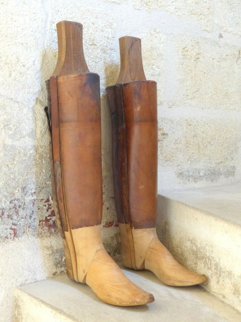 May include: Two wooden boot forms with leather uppers. The forms are made of light brown wood and have a pointed toe. The leather uppers are a dark brown color.
