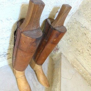 May include: Two wooden boot forms, one brown and one light brown, with a light brown wooden base. The forms are made of wood and have a smooth finish.
